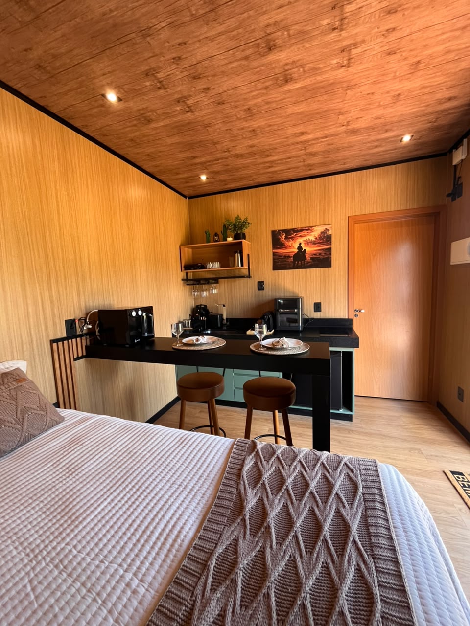 Interior da unidade visto da cama, com cozinha compacta ao fundo