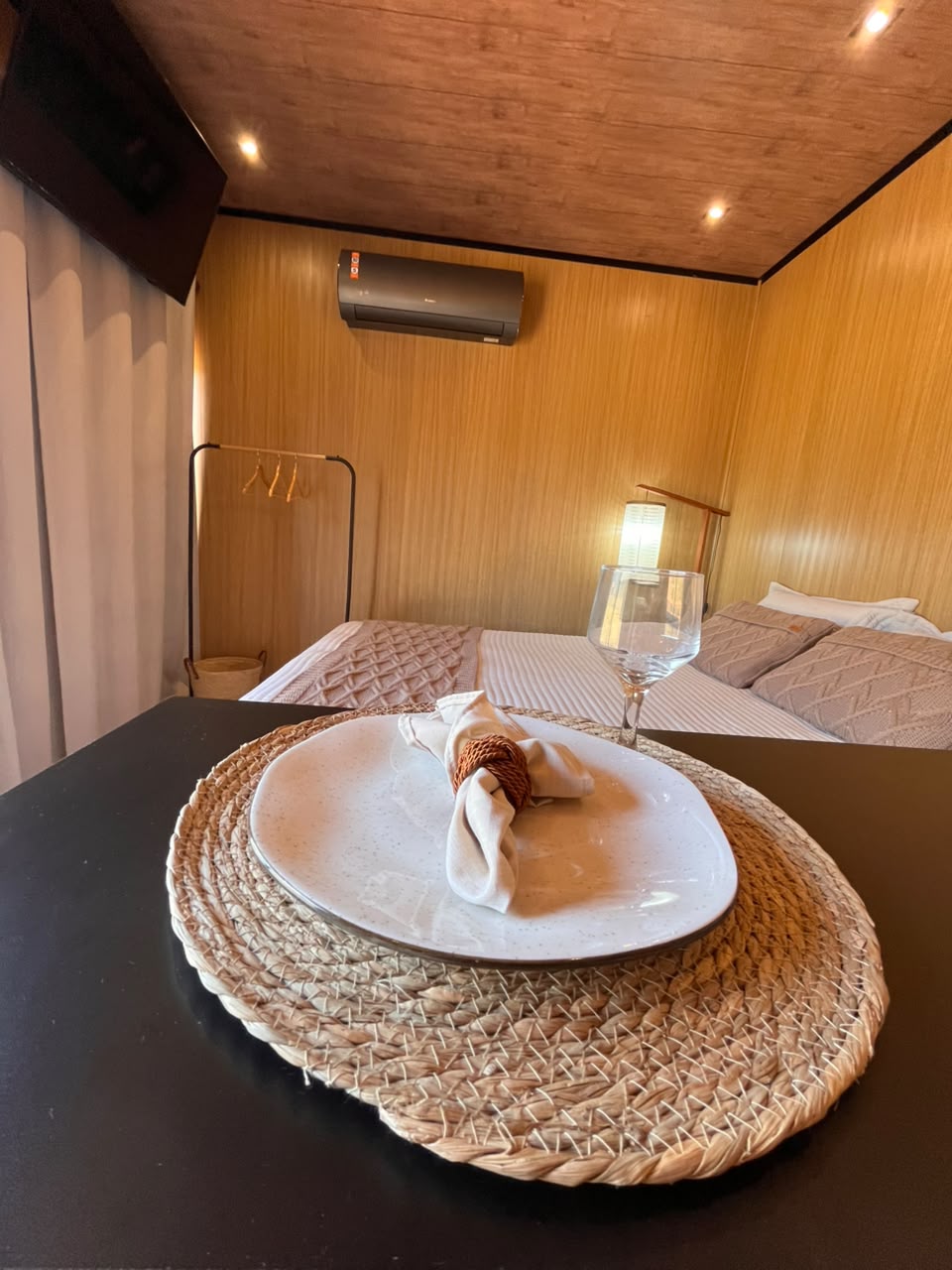 Mesa posta com taça sob luz baixa, com a cama ao fundo